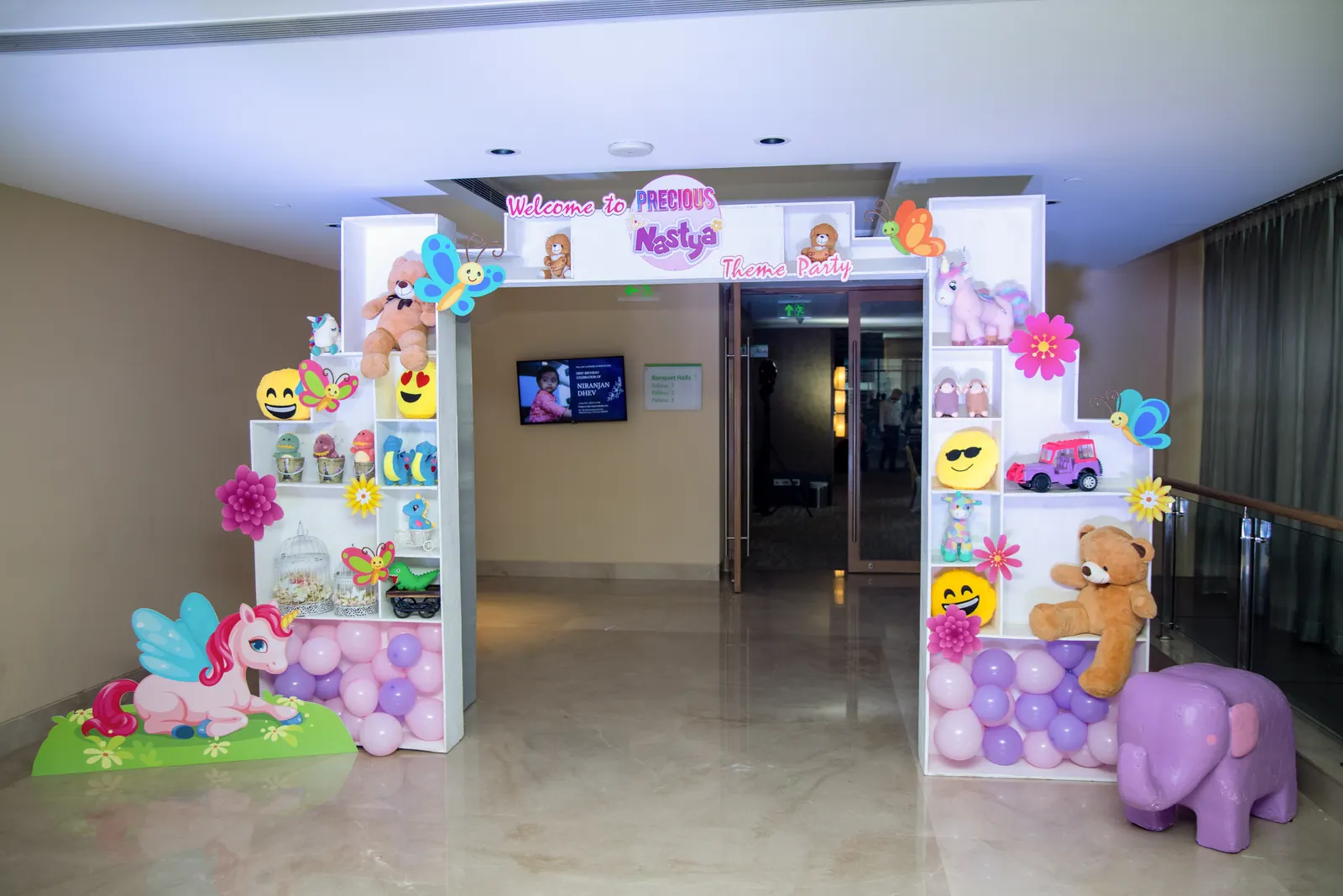 Soft-toy themed entrance with white display shelves of teddies and plush toys, unicorn cut-outs and pastel balloon fills