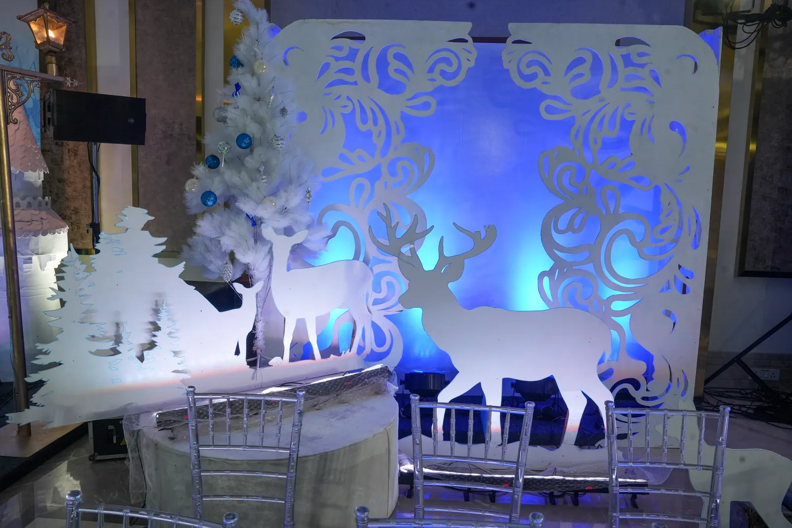 Winter themed photo corner with laser-cut reindeer and snowflake panels, a white Christmas tree and blue uplighting